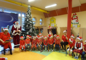 Grupa dzieci siedzi na krzesełkach wokół pani dyrektor Marii Królikowskiej, która czyta legendę o świętym Mikołaju.